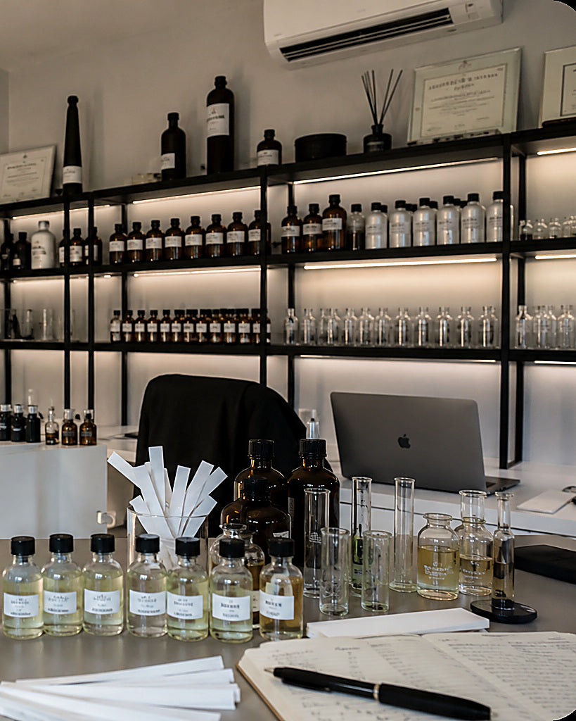 The Yevfumes studio shelving, arranged with amber and clear glass bottles of raw materials, beside the formulation bench